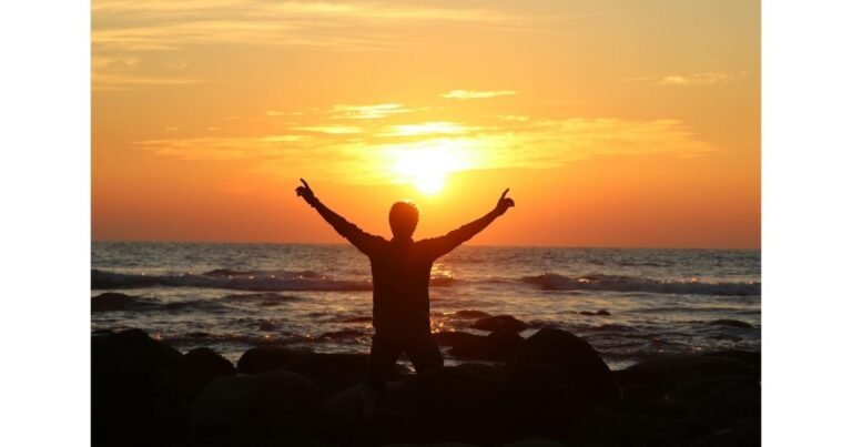 Silhouette of a person lifting their hands toward the sunrise over the ocean, symbolizing worship, gratitude, and a godly lifestyle